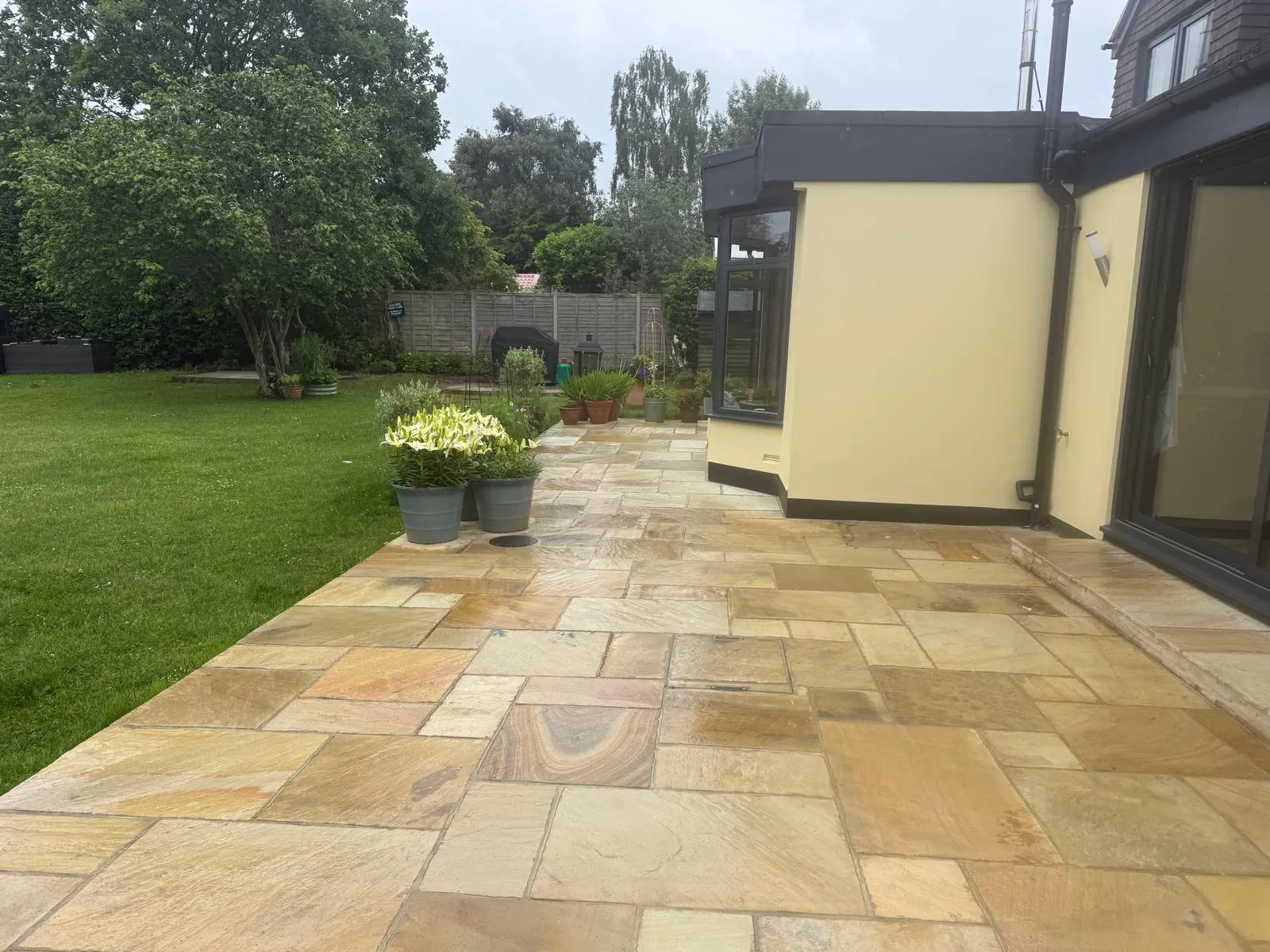 Riven Indian sandstone patio with potted lilies beside a striped lawn in Downe Village