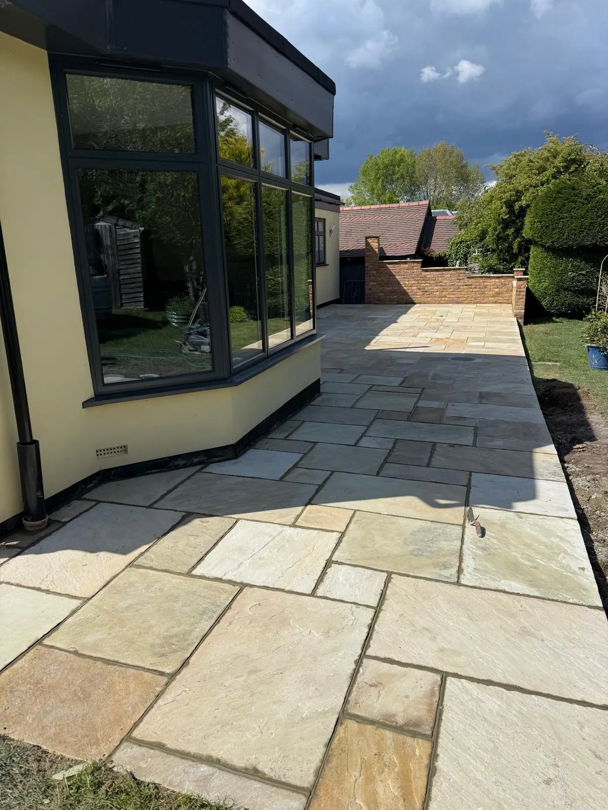 Indian sandstone paving curving around a bay window on a rendered house in Downe Village