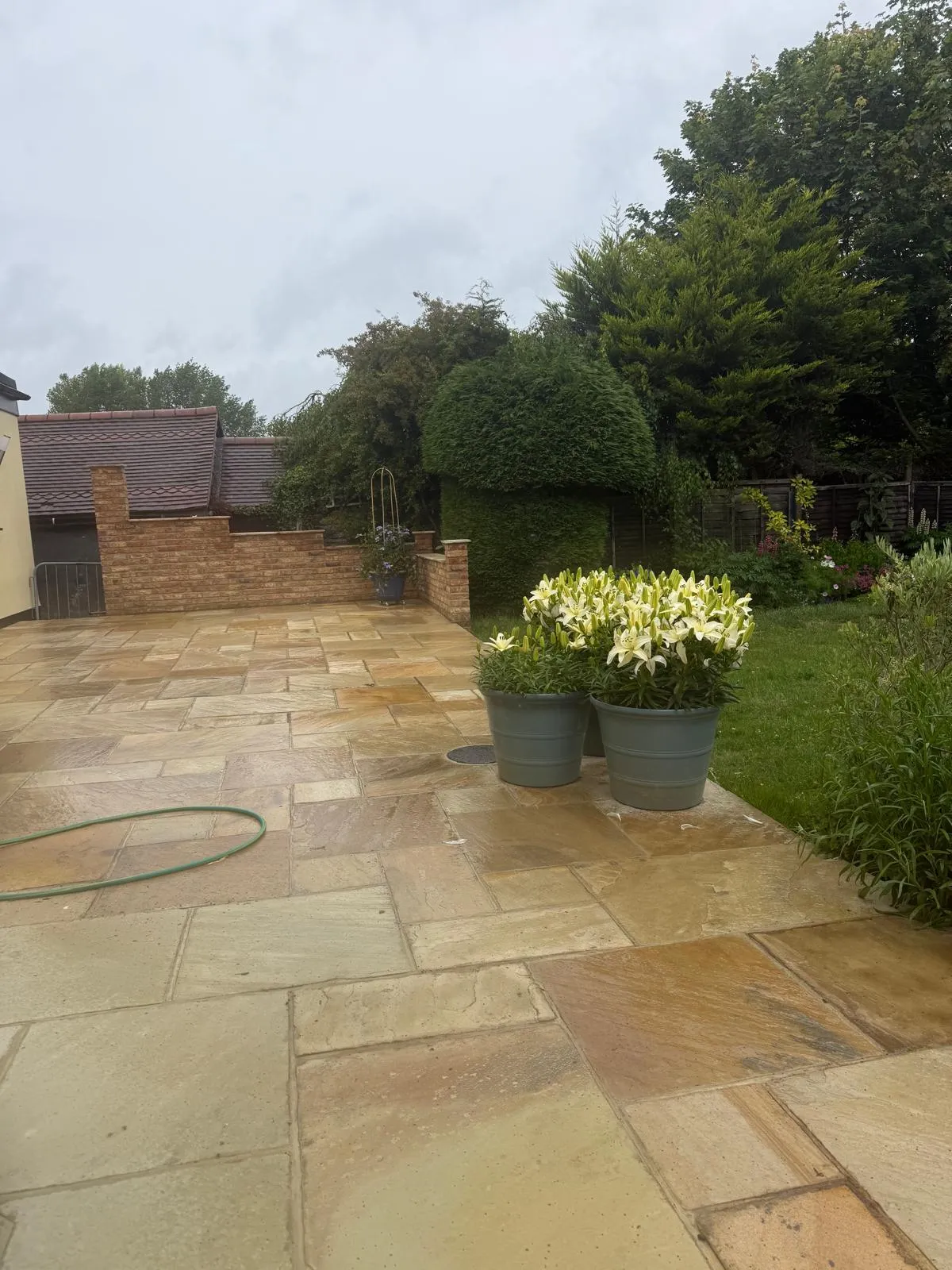Indian sandstone patio with potted white lilies and mature trees behind in Downe Village