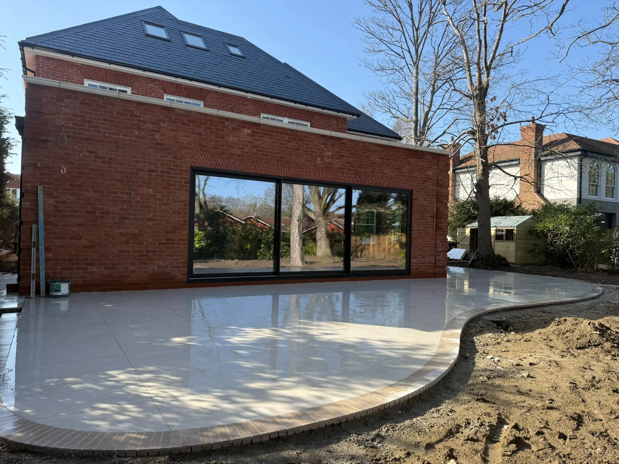 Cream porcelain patio with curved brick border laid by Prestige Landscapes beside a modern brick extension