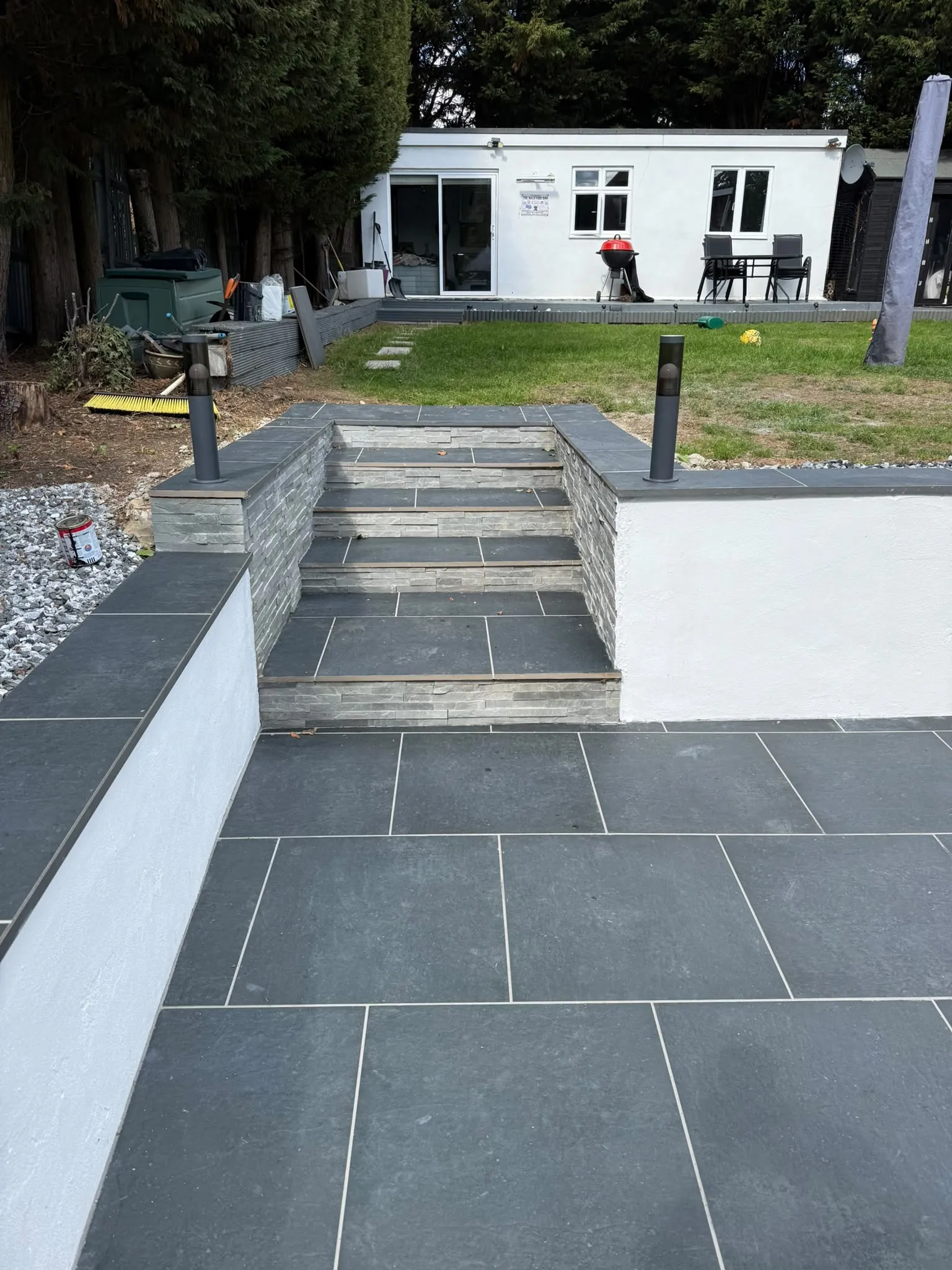 Dark porcelain patio with split-face stone steps and bollard lighting by Prestige Landscapes
