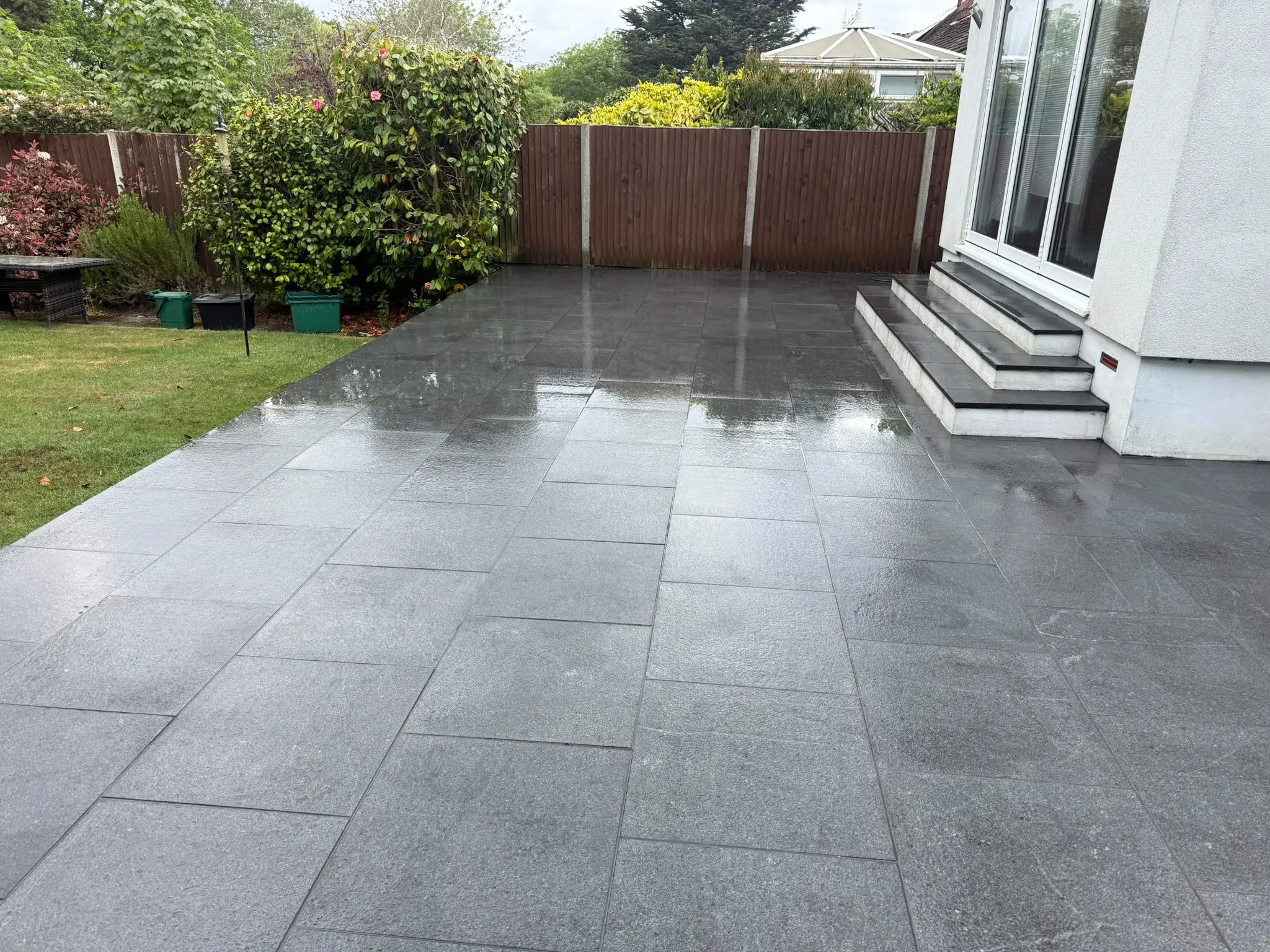 Charcoal granite patio beside a white rendered house by Prestige Landscapes