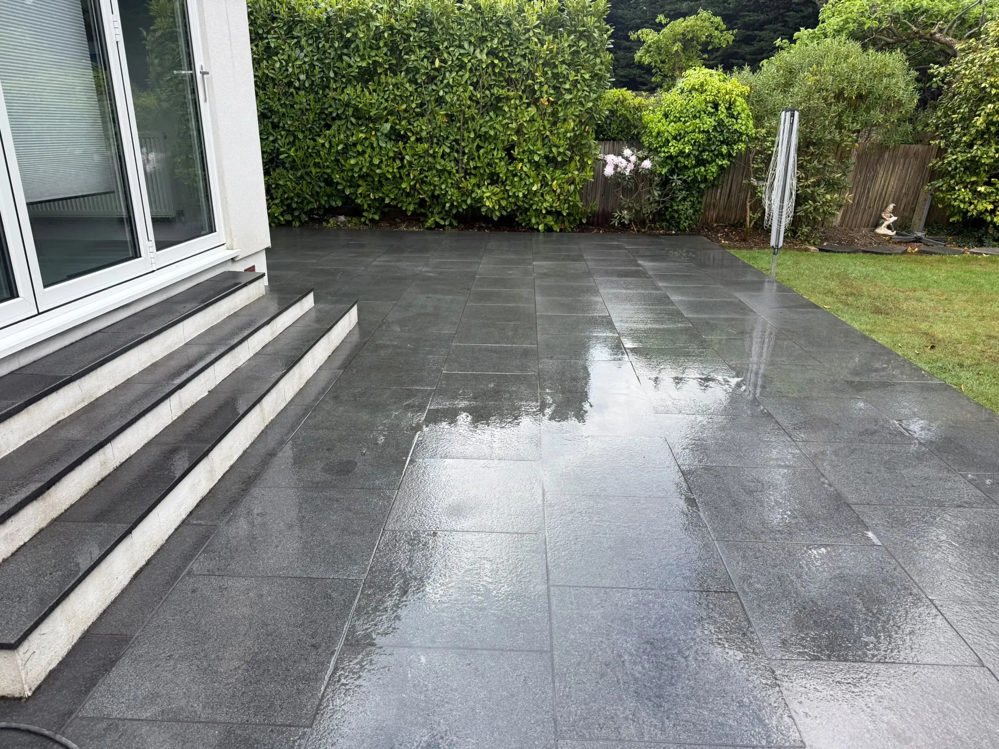 Dark granite patio with steps and laurel hedge laid by Prestige Landscapes