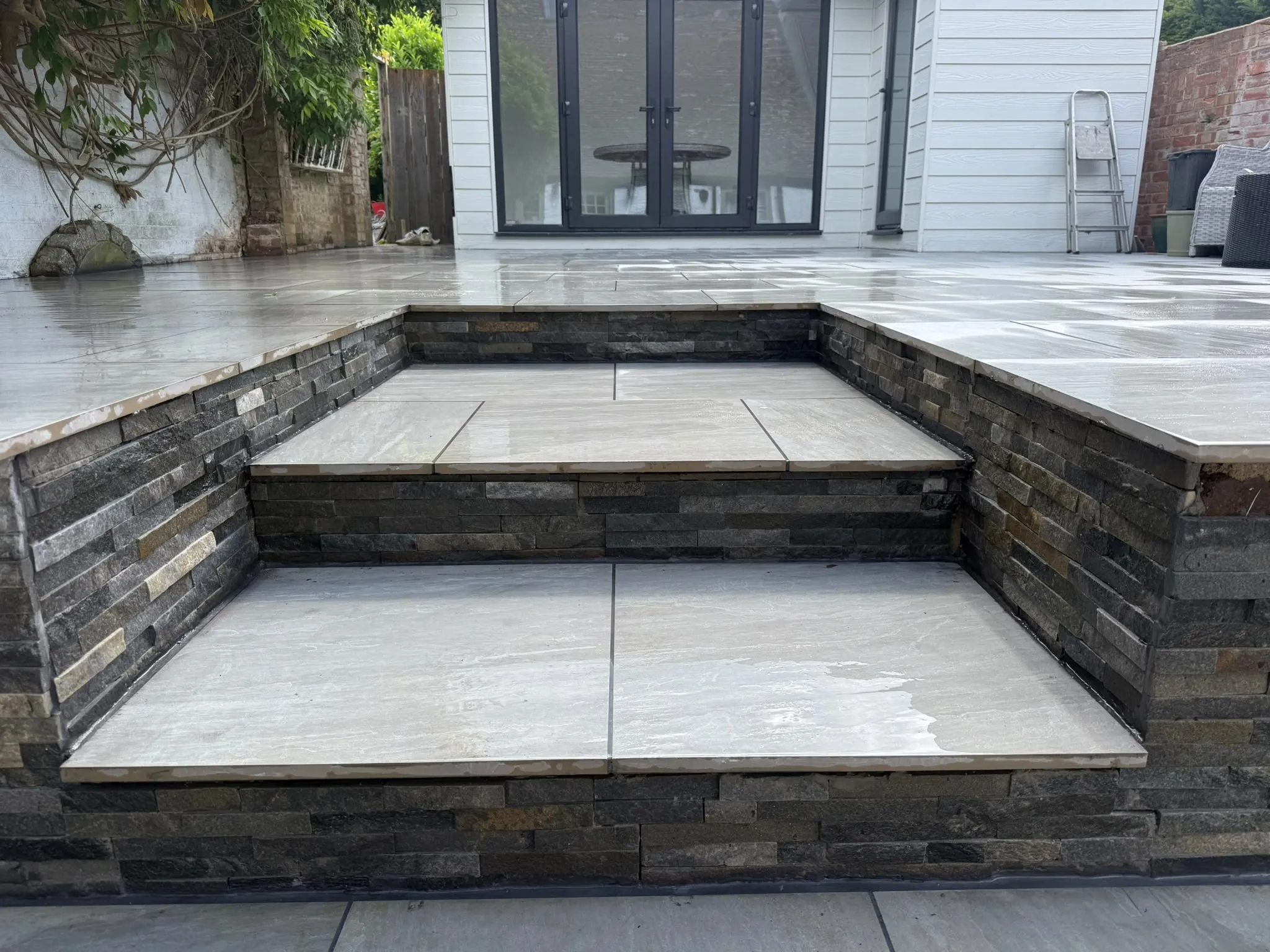 Split-level porcelain patio with split-face stone steps by Prestige Landscapes