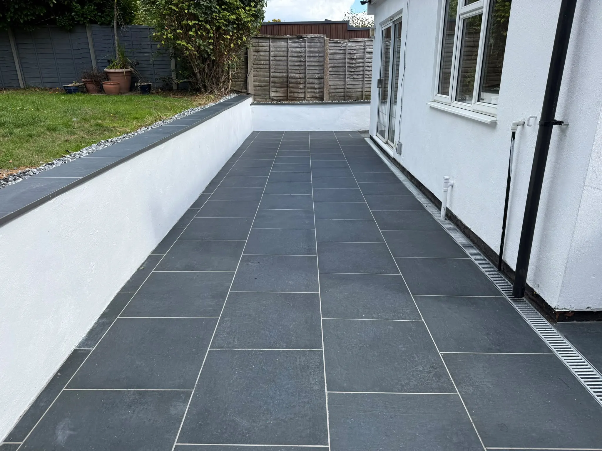 Charcoal porcelain side patio with rendered raised wall by Prestige Landscapes