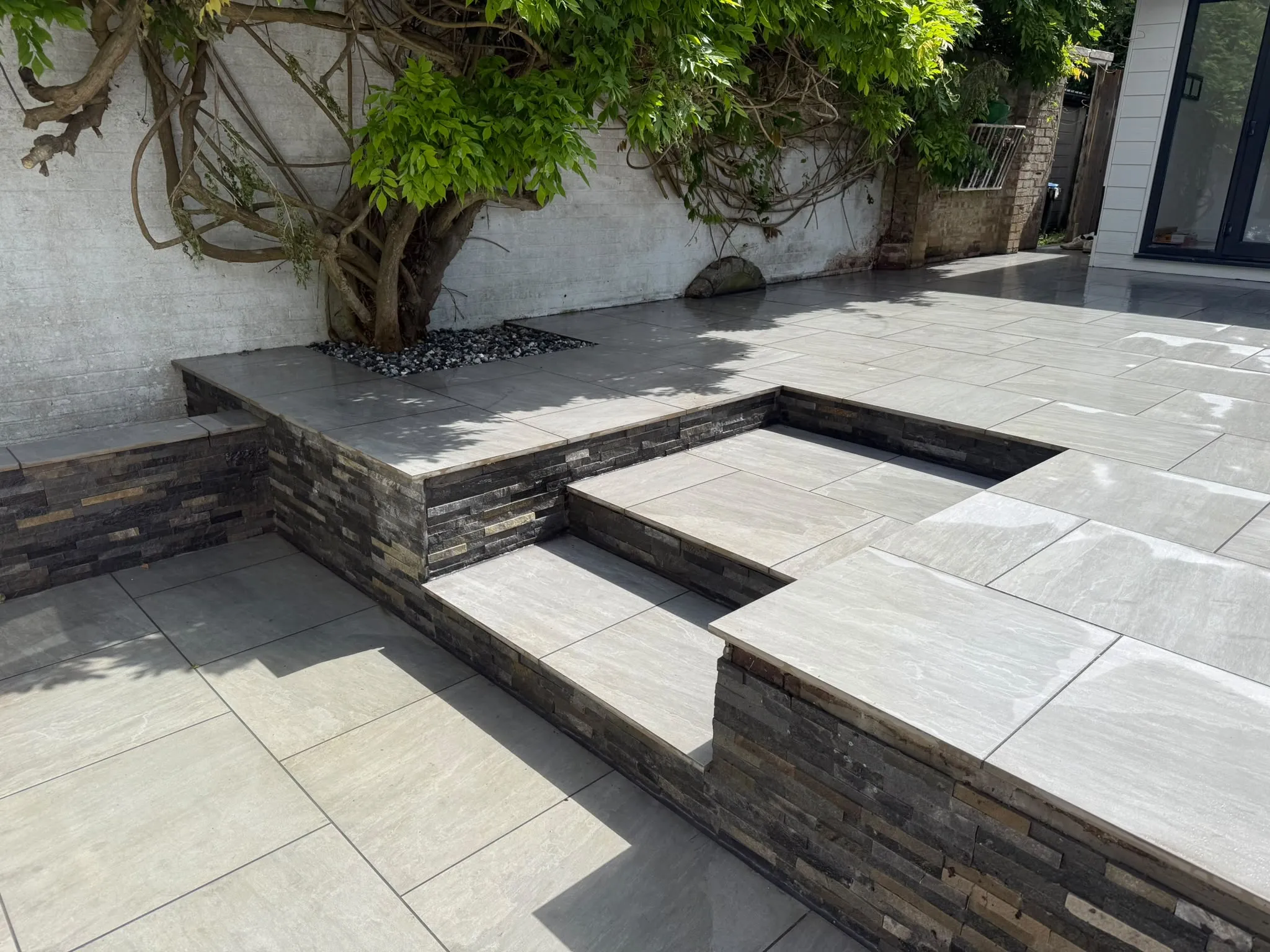 Grey porcelain patio with split-face stone raised beds by Prestige Landscapes