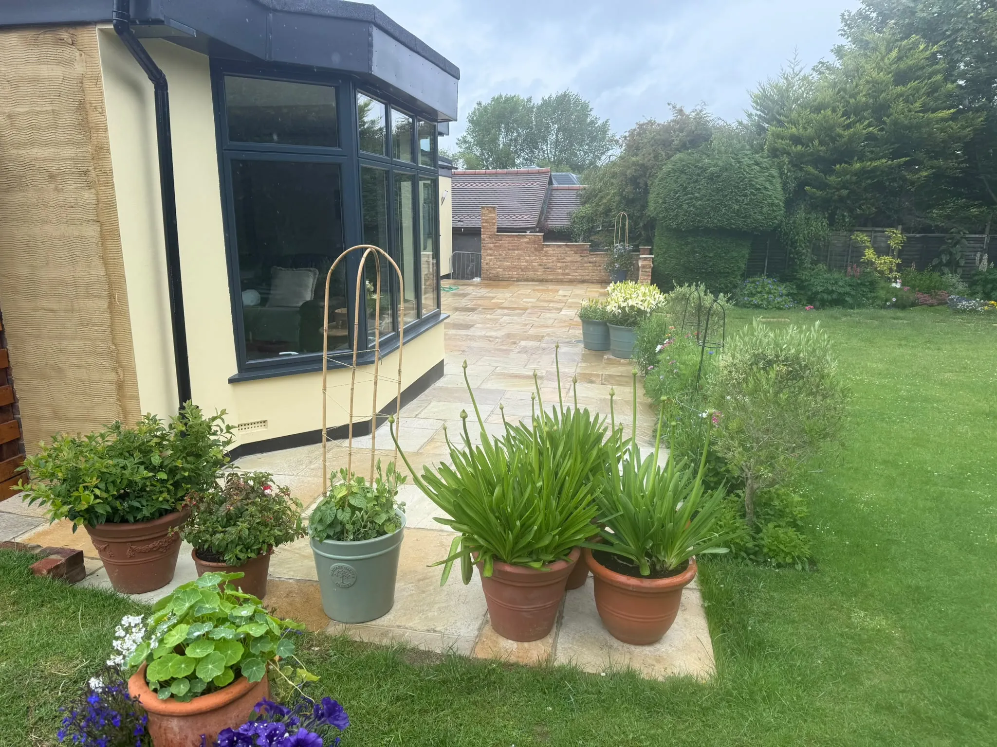 Indian sandstone patio and borders beside a bay-fronted home by Prestige Landscapes