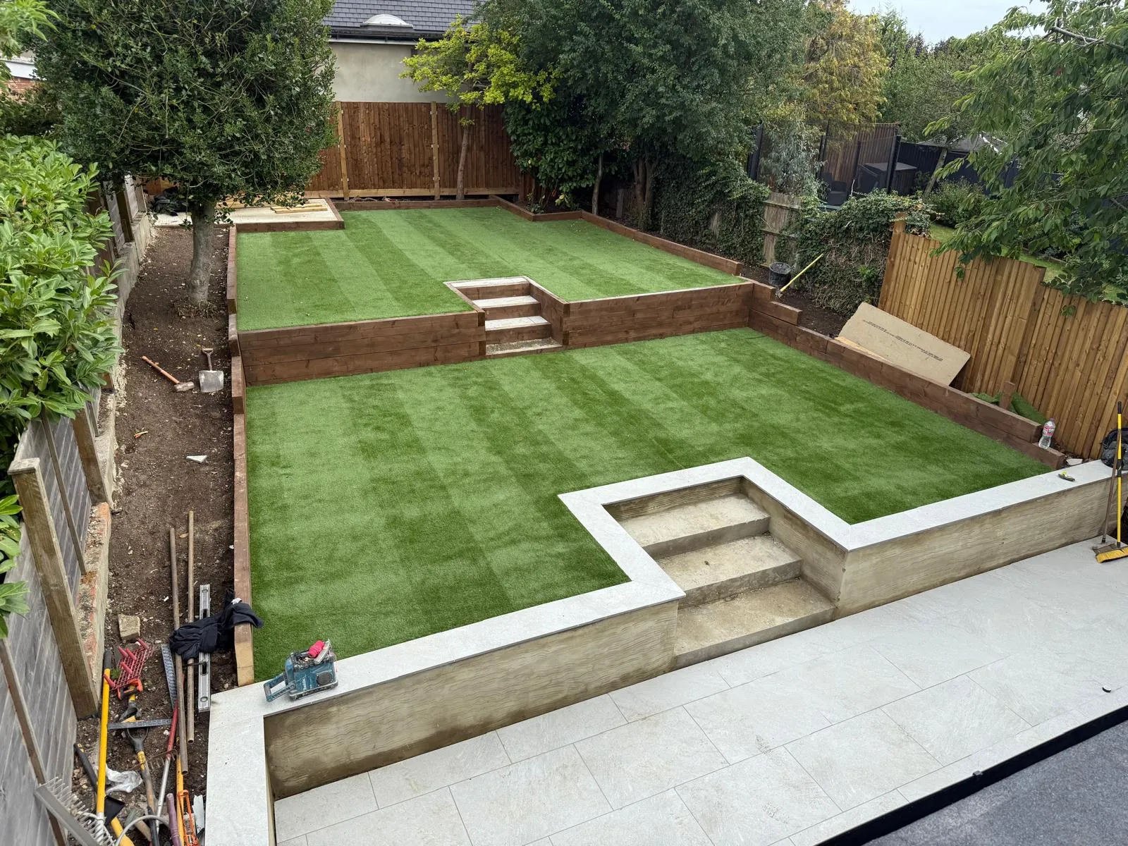 Split-level artificial grass garden with sleeper walls by Prestige Landscapes
