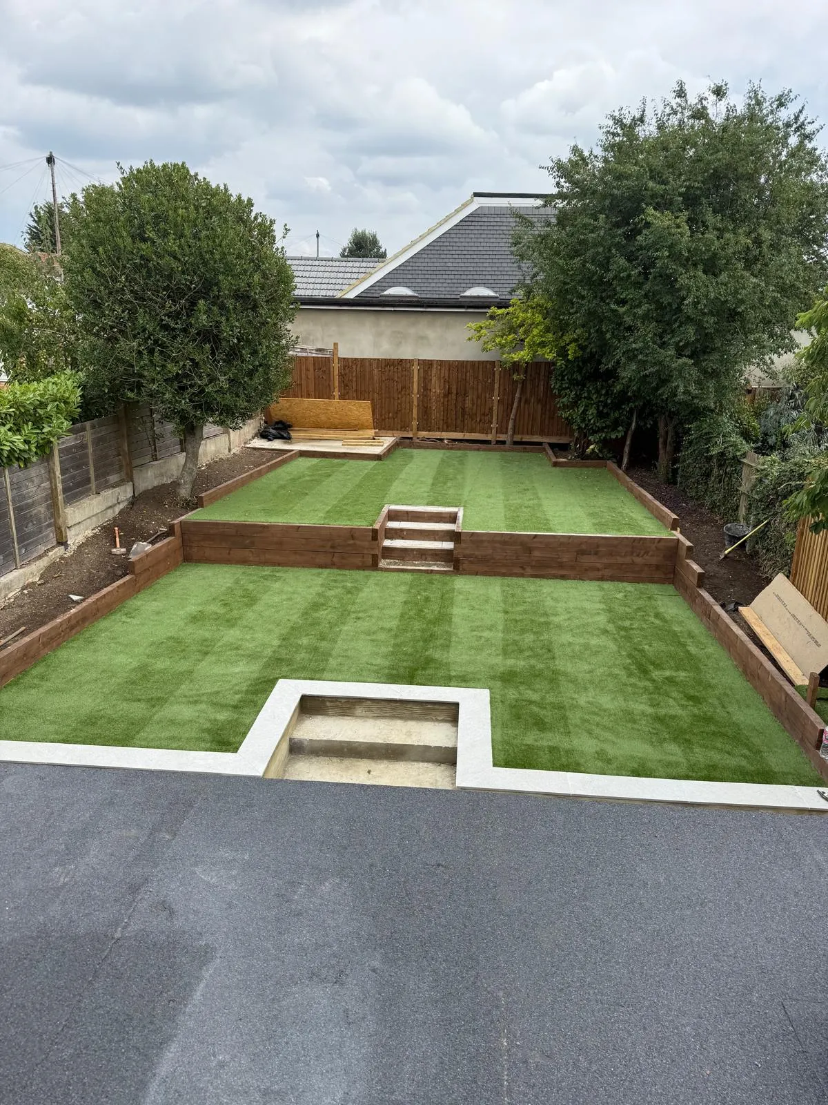 Tiered artificial grass garden with sleeper retaining walls by Prestige Landscapes