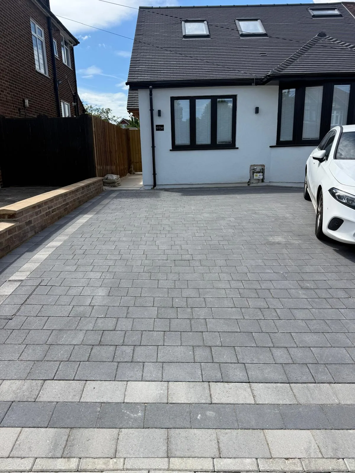 Grey block paving driveway to a rendered home by Prestige Landscapes