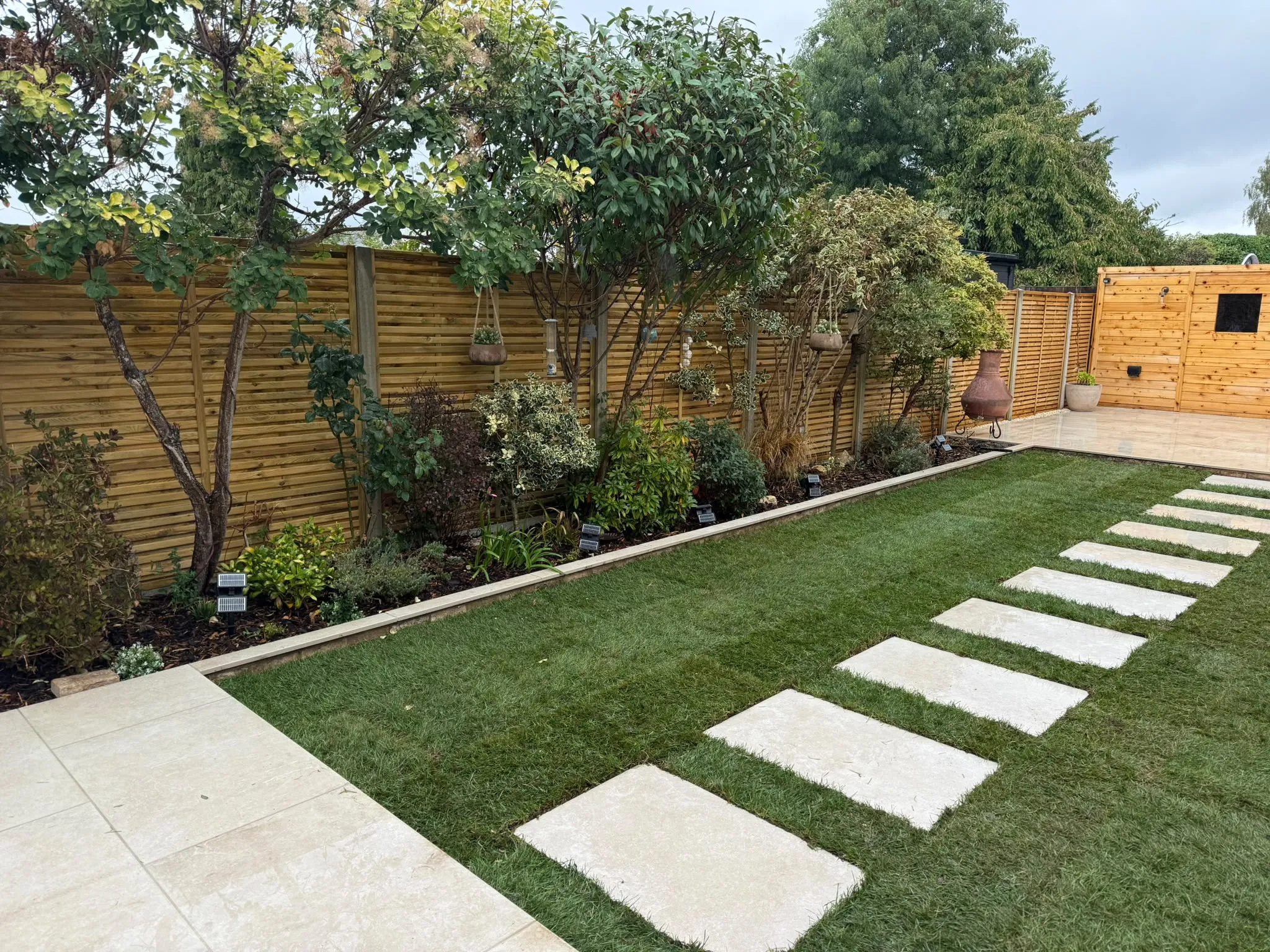 Finished Beckenham garden with porcelain patio, artificial lawn and stepping-stones by Prestige Landscapes